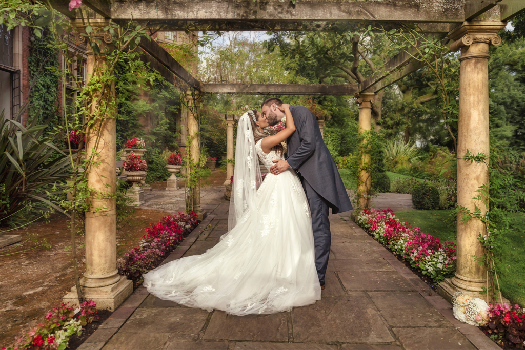 bride & groom kissing under a beautiful flower covered archway