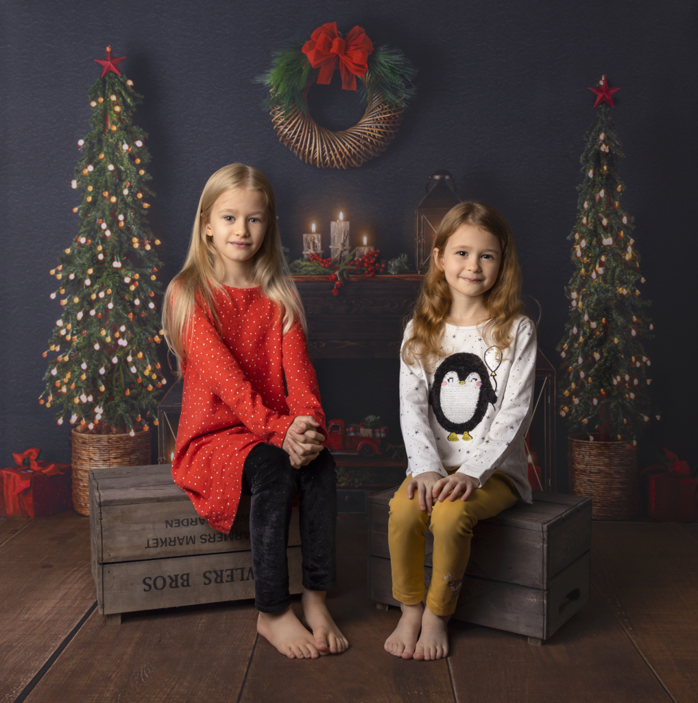 Girls sitting in front of beutiful Christmas fireplace scene for Christmas mini session 2021